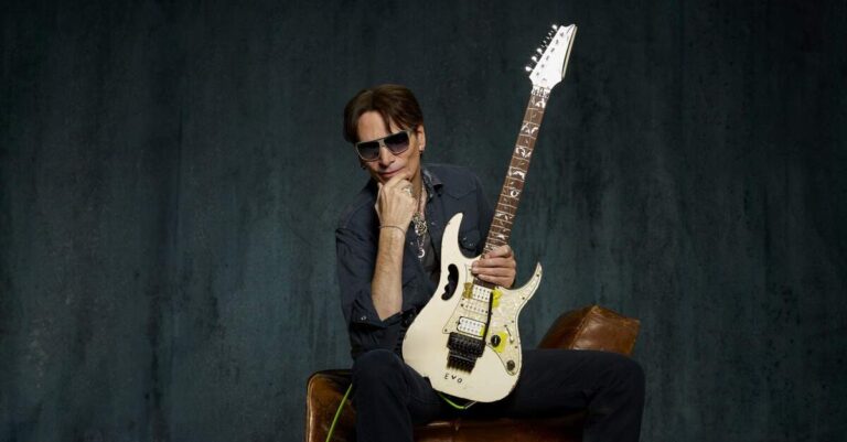 Steve Vai sentado em um sofá com uma guitarra Ibanez