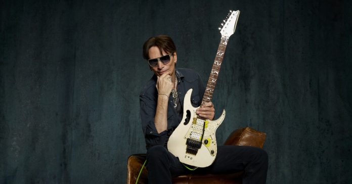 steve-vai Steve Vai sentado em um sofá com uma guitarra Ibanez