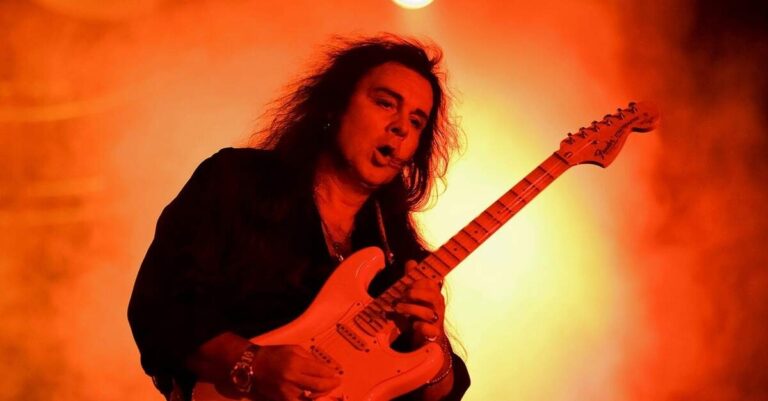 Malmsteen tocando com uma Fender em um palco iluminado